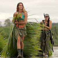 Three women holding leaves on a beach
