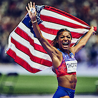 Gabby Thomas celebrating while holding the American flag.