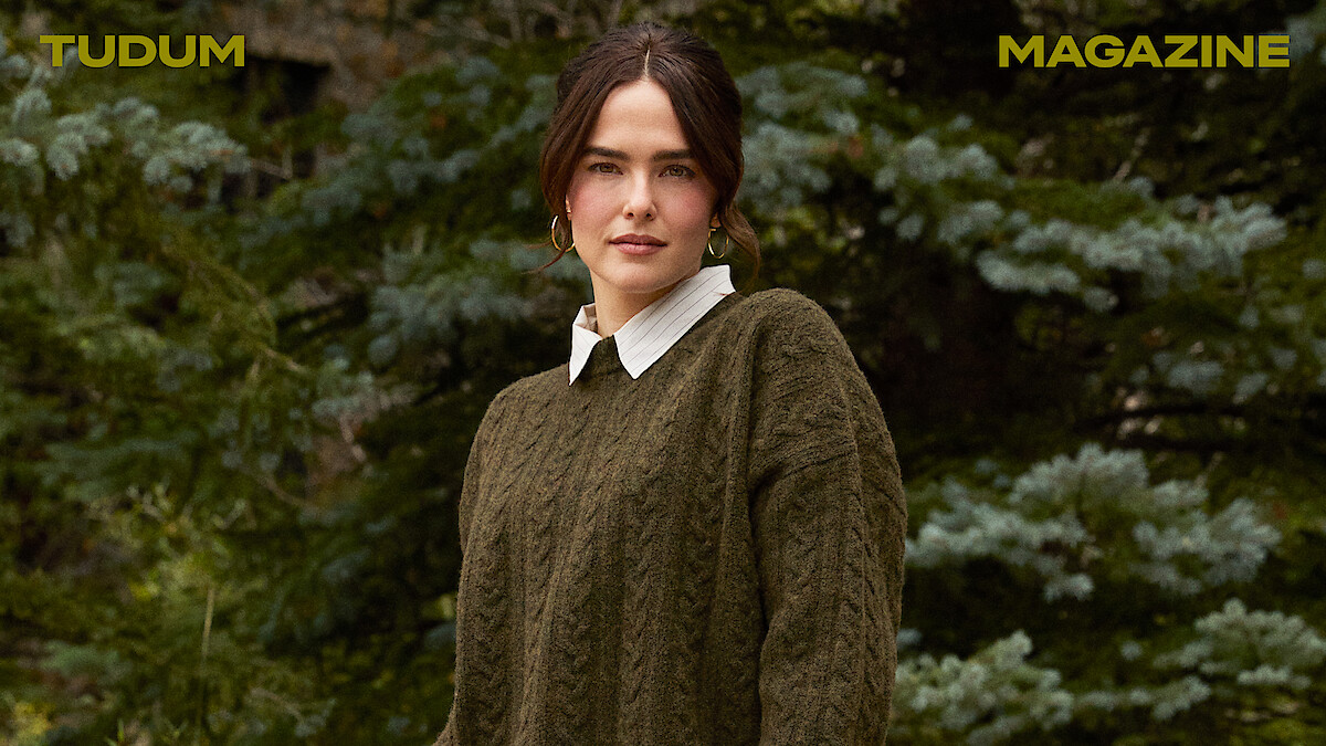 Zoey Deutch stands against a backdrop of trees