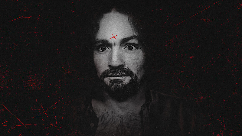 A man with curly hair and a beard stares intensely at the camera, set against a dark, gritty background. He has a red X marked on his forehead and visible chest hair, wearing an open shirt. The overall mood is eerie and dramatic.