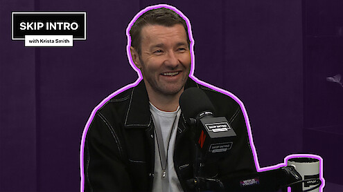 Joel Edgerton sits smiling in front of a microphone during a podcast recording for "Skip Intro with Krista Smith." The background is purple, and the podcast logo appears in the top left corner.