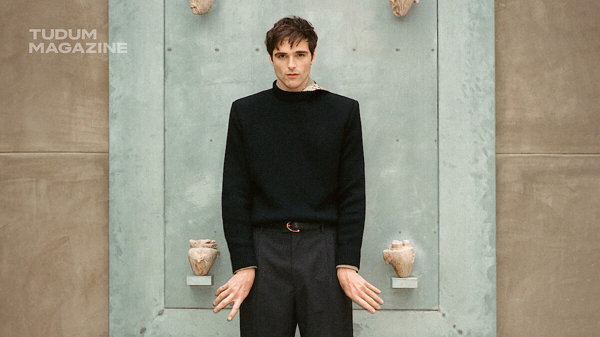 Jacob Elordi stands in front of a blue door while dressed in black.