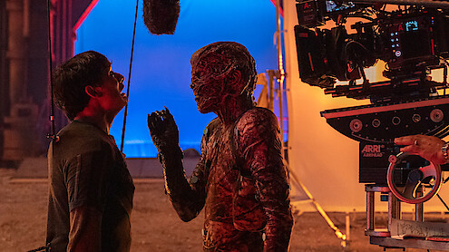 Ator com maquiagem de monstro encara outro ator em um set de filmagem, criando uma atmosfera intensa de bastidores.
