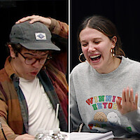 Gaten Matarazzo and Millie Bobby Brown sit at a table with scripts and microphones, laughing and reacting animatedly, in a casual, creative studio environment suggesting a lively script reading or rehearsal session.