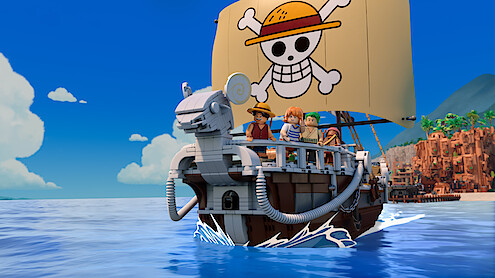 LEGO pirate ship with four minifigures sailing on blue water, featuring a sail with a skull and crossbones wearing a straw hat, under a clear blue sky with a coastline and mountains visible in the background.