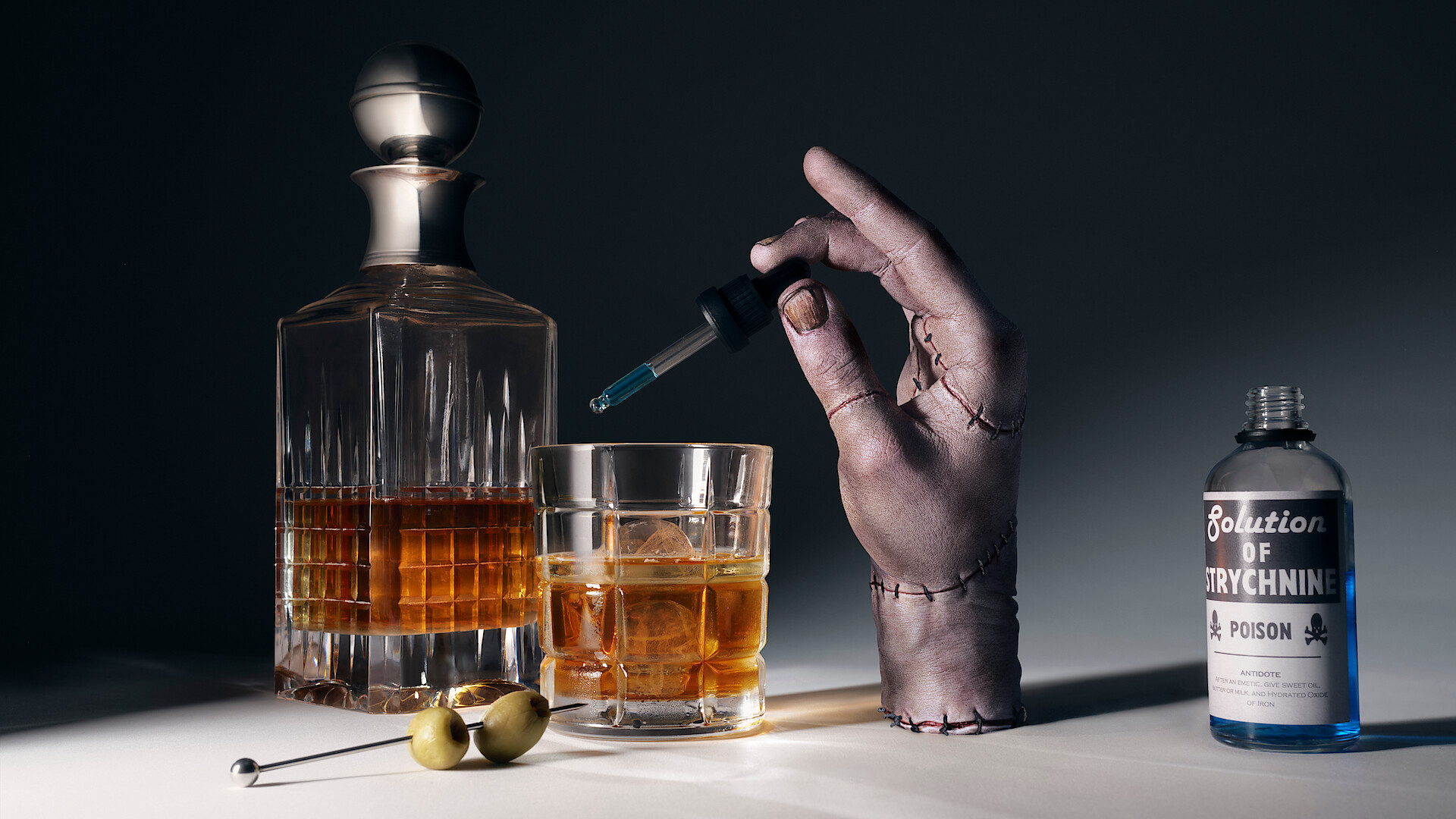 Thing holding a dropper of poision over a glass of whiskey.