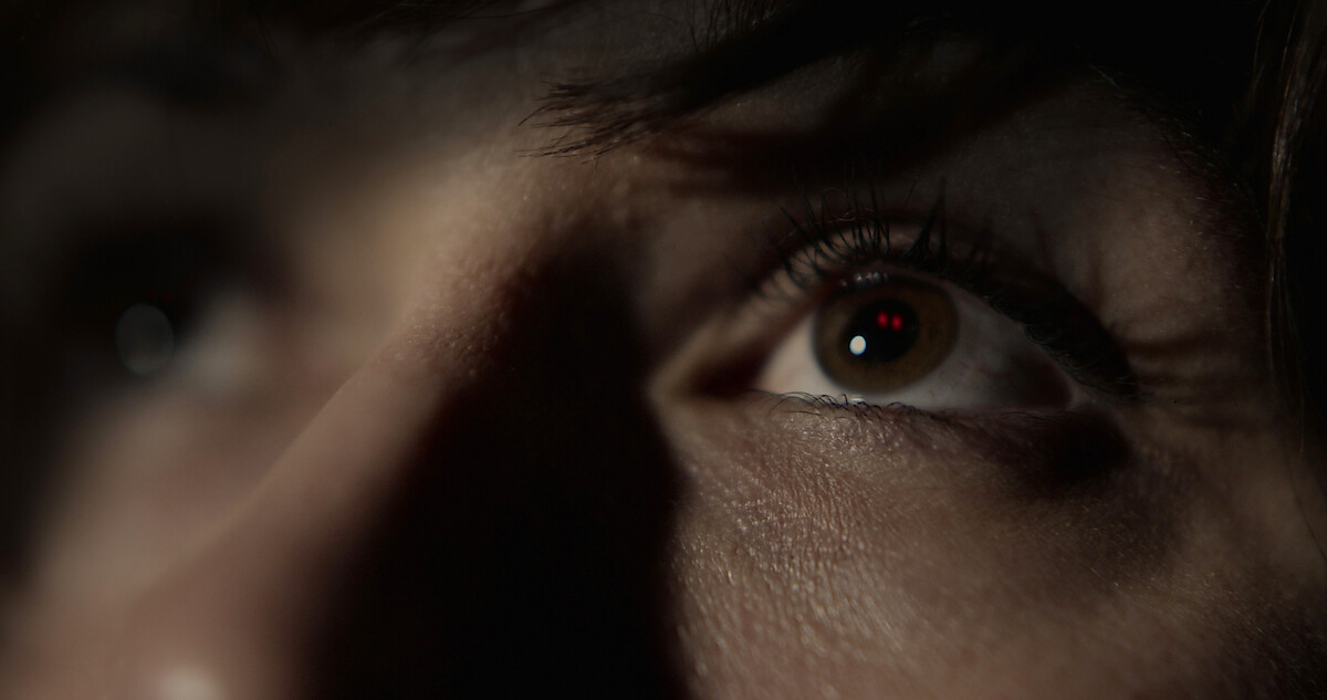 A red eyed figure appears reflected in a women's eyes.