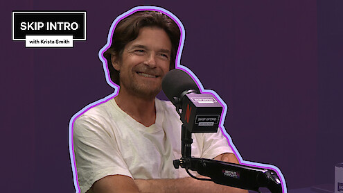 Jason Bateman smiles while speaking into a microphone on the 'Skip Intro with Krista Smith' podcast.