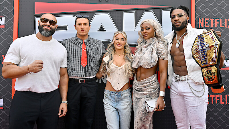 Rusev, Kit Wilson, Tiffany Stratton, Jade Cargill, and Trick Williams posing together on a red carpet at a WWE RAW event, with a branded backdrop. One person is holding an NXT Championship belt. The group is dressed in trendy and distinctive outfits.