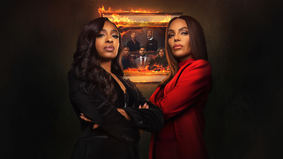 Two women in formal suits stand confidently with arms crossed in front of a burning framed portrait showing a group of people, set against a dark background, creating a dramatic and intense atmosphere.
