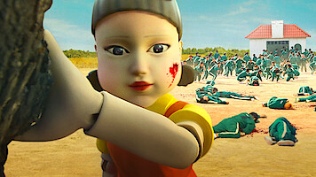 A large doll with blood on her cheek turns her head with people in green jumpsuits running away behind her in Season 1 of 'Squid Game'