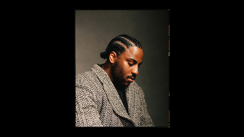 Malcolm Washington wears a patterned coat and sits in profile.