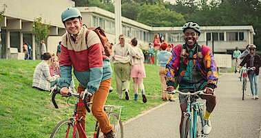 Asa Butterfield as Otis and Ncuti Gatwa as Eric ride their bikes to school in Season 4 of 'Sex Education.'