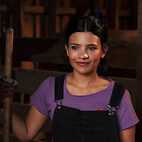 Nikki Rodriguez as Jackie wearing overalls in a barn in 'My Life with the Walter Boys' Season 2.