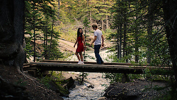 Jackie and Cole walk across a bridge in a forest