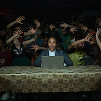 Rita (Zoe Saldaña) has her arm outstretched as she dances in a red velvet blazer and t-shirt in a dark ballroom. 
