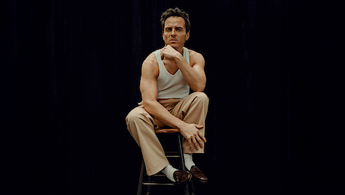 Andrew Scott wears khakis, a white tank, loafers, and a blazer or coat draped over his shoulders.