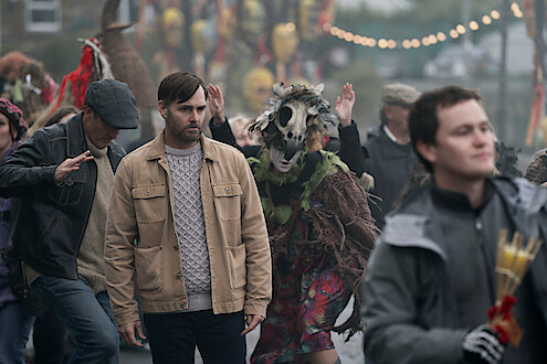 Will Forte as Gilbert Power walks through a crowd at a festival in 'Bodkin'
