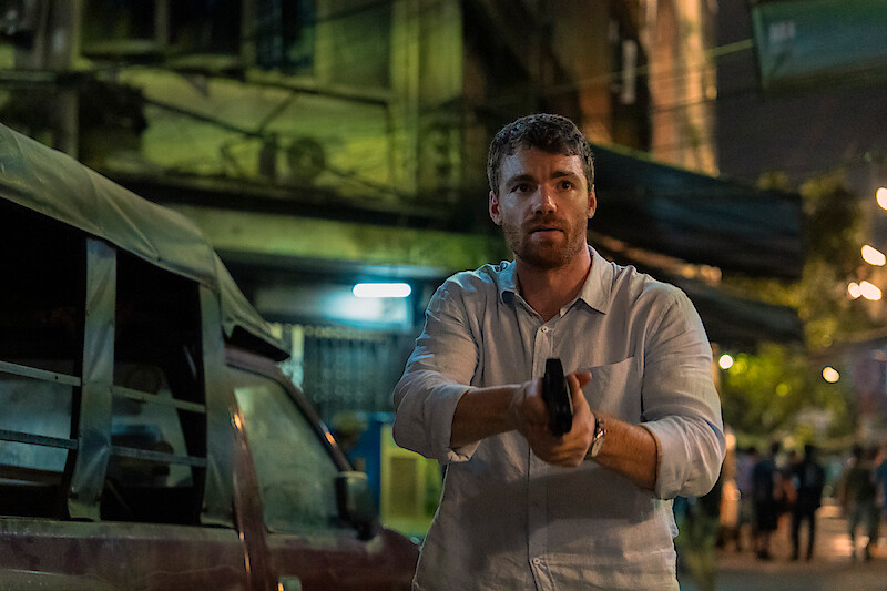 Gabriel Basso como Peter Sutherland com uma arma na mão.