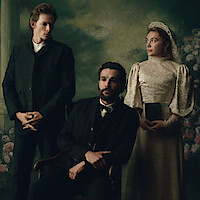 Three people in vintage formal attire pose indoors against a painted floral backdrop; a seated man in a suit is flanked by a standing man and woman in a lace dress with a tiara, holding a book, evoking an old-fashioned, solemn portrait.