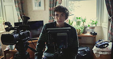 Samuel Blenkin as XX sits behind a video camera with headphones on in Season 6 of Black Mirror.