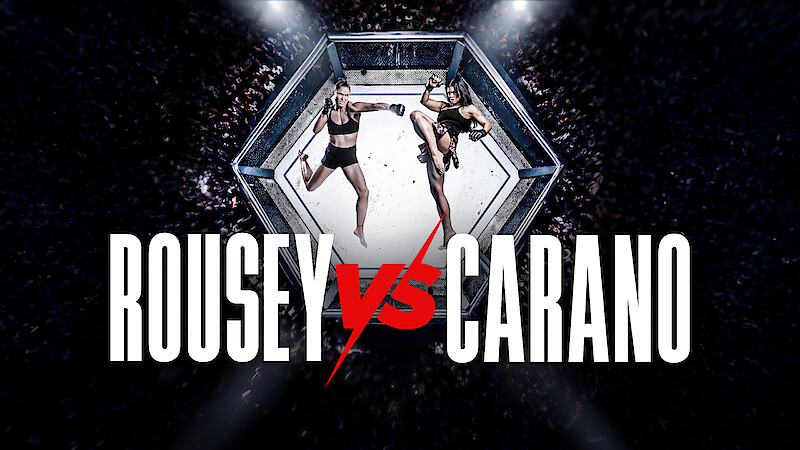 Two female fighters facing off in a mixed martial arts octagon cage, surrounded by a cheering crowd, with large text reading Rousey vs Carano in front.