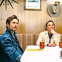 Glen Powell and Richard Linklater sit at a restaurant booth together.