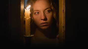 Woman with curly hair peering through a partially open door, illuminated by candlelight in a dark, dimly lit setting, creating a tense and mysterious atmosphere.