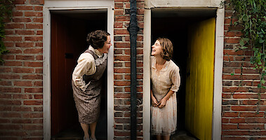 Two neighbors lean out of their doorways and smile at each other in 'Wicked Little Letters'