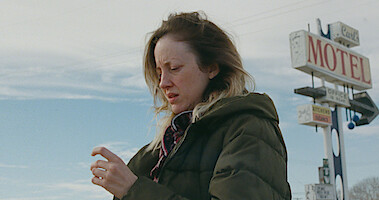 Woman in coat standing outside motel sign.