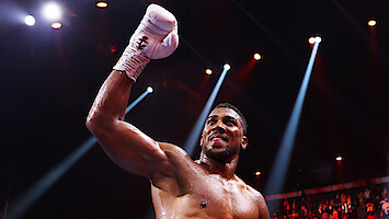 Boxer in a ring celebrates with a raised, gloved fist under dramatic arena lighting, surrounded by a cheering crowd, capturing a victorious and energetic mood.