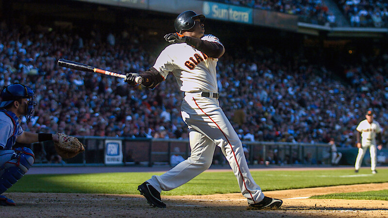 Barry Bonds in a Giants uniform swinging bat during a sunny game, catcher and umpire nearby, large crowd in stadium background.