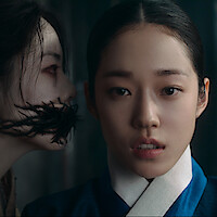 Two women indoors, one in traditional clothing looking ahead with concern, the other with ghostly features and a mouth of black branches, creating a tense, eerie atmosphere.