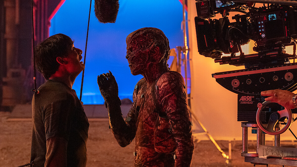 Ator com maquiagem de monstro encara outro ator em um set de filmagem, criando uma atmosfera intensa de bastidores.