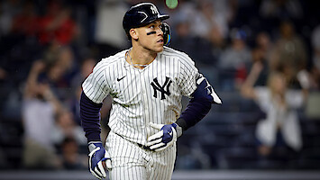 New York Yankees baseball player in pinstripe uniform runs on field during a night game; blurred crowd in the background creates an energetic, competitive atmosphere.