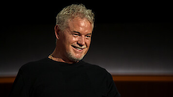 Eric Dane sits wearing a black shirt against a black backdrop.