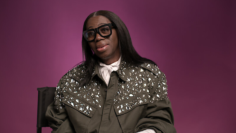 J. Alexander aka Miss J sitting in front of a plum background