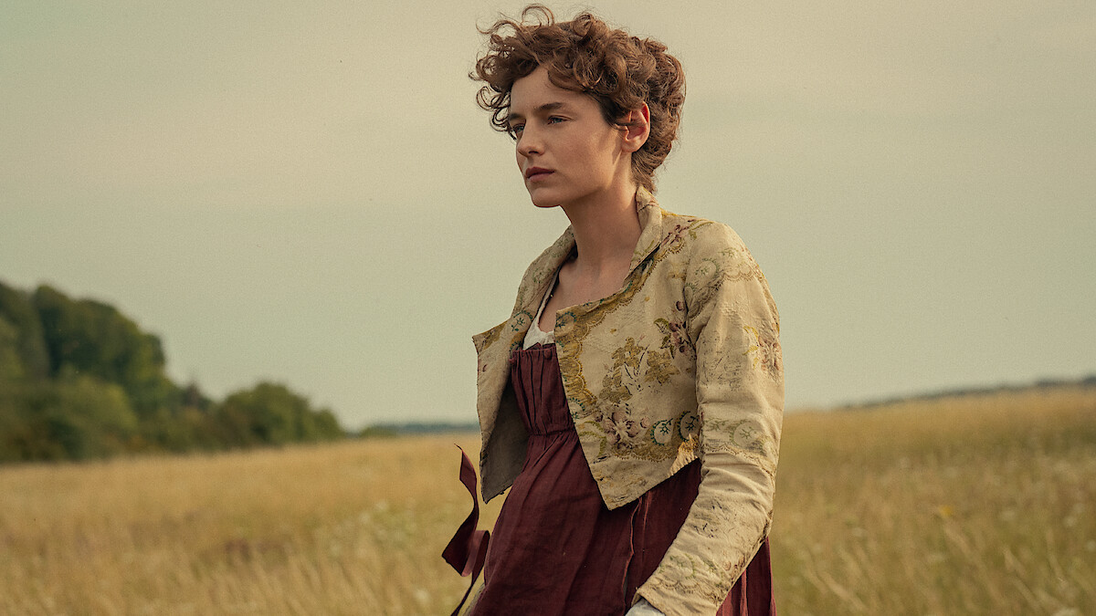 Woman in historical dress standing in a field with tall grass, trees in the background, and a cloudy sky, creating a calm, pastoral setting.