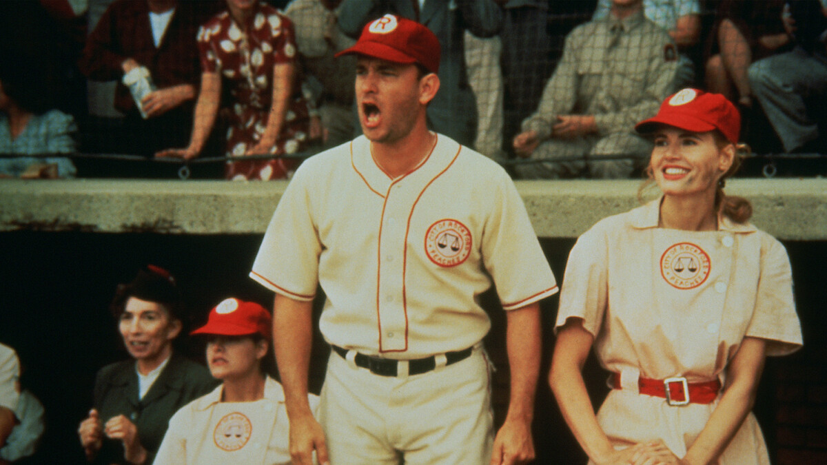 Baseball players in vintage uniforms, including a man shouting and a woman smiling, stand near a dugout; spectators watch from the stands, creating a lively, nostalgic sports atmosphere at a ballpark.