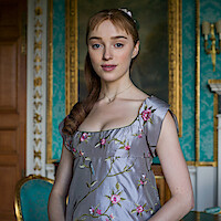 Phoebe Dynevor as Daphne Bridgerton in a lavender, floral embroidered Regency dress stands in an ornate room with teal wallpaper, gold-framed mirror, chandelier, and marble fireplace.