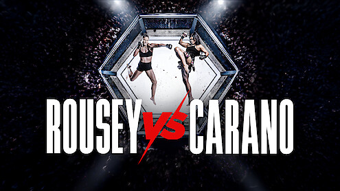 Two female fighters facing off in a mixed martial arts octagon cage, surrounded by a cheering crowd, with large text reading Rousey vs Carano in front.