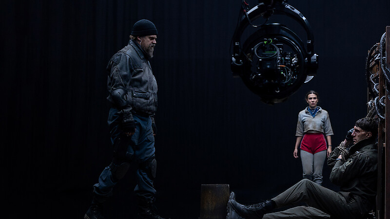 Cena tensa em um set de filmagem com três atores e um grande equipamento de câmera.