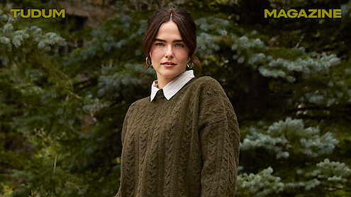 Zoey Deutch stands against a backdrop of trees