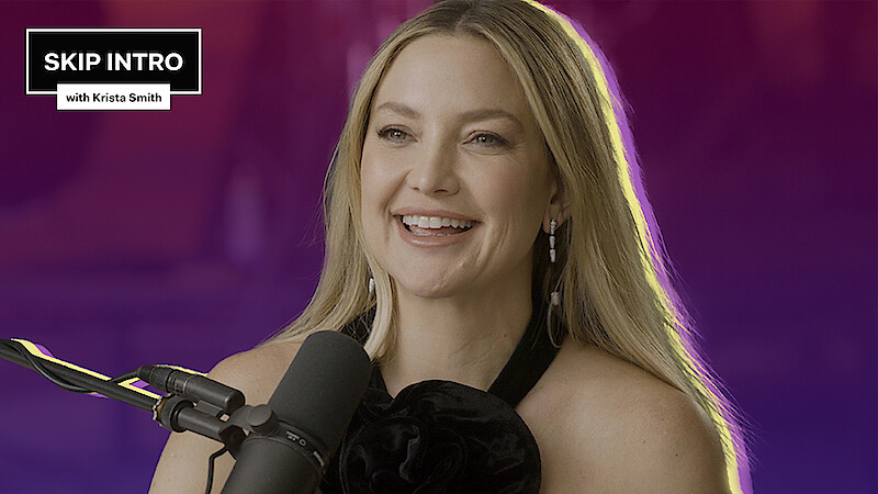 Kate Hudson is smiling as she sits in front of a microphone.