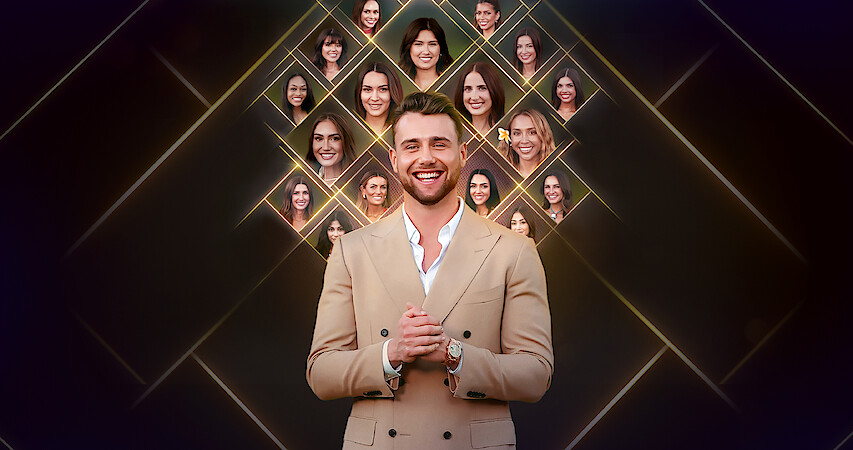 A smiling man in a tan suit stands in front of a dark background with glowing diamond shapes featuring multiple women’s faces displayed above and behind him, suggesting a reality TV or dating show setting.