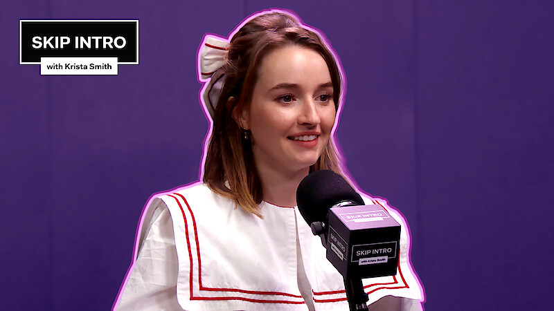 Kaitlyn Dever, smiling warmly, is seated in front of a microphone.
