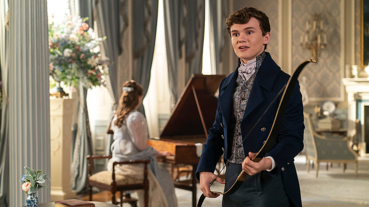 Will Tilston as Gregory Bridgerton in Regency attire holding a bow in an elegant, classic drawing room.
