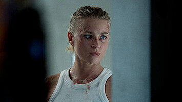 Jeanne Goursaud stands in close up with bloody cuts on her face and blood spots on her white tank top in an image from 'Exterritorial.'