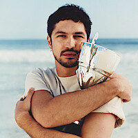 Gabriel Leone wears a white t-shirt and clutches a trophy to his chest.