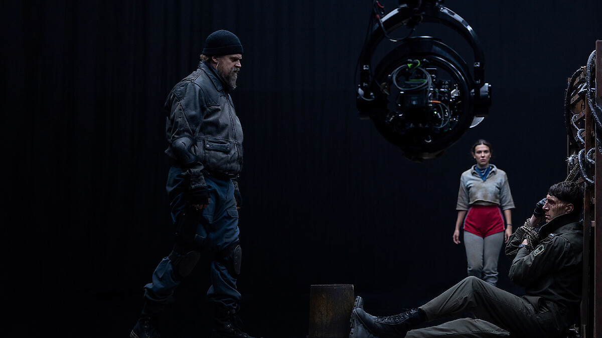 Cena tensa em um set de filmagem com três atores e um grande equipamento de câmera.